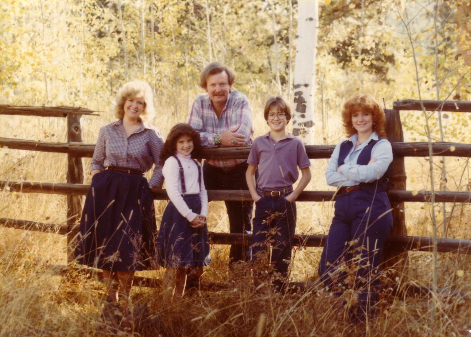 The Childers family standing at a wooden fence among aspen trees