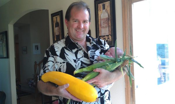 Will holding a giant yellow squash, ears of corn, and his newborn